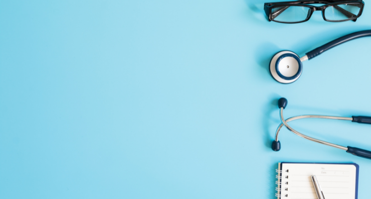 stethoscope, glasses, paper and pen against blue background