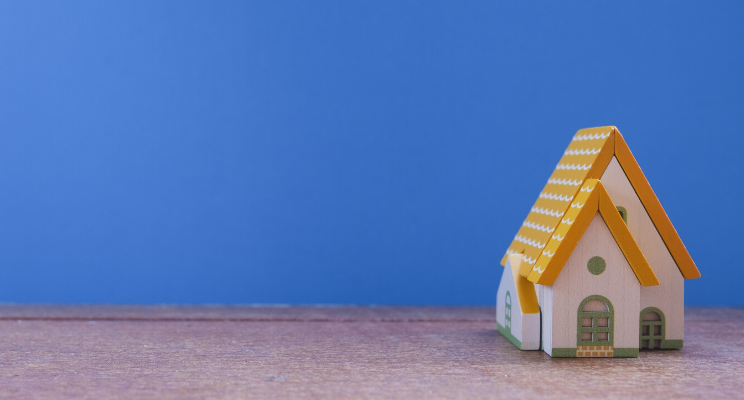 miniature house on wooden table next to blue background