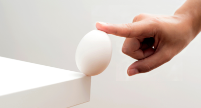 finger holding a single egg from falling from a white table